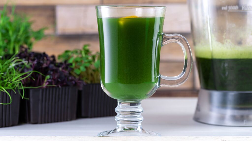 Glass of Green Barley Juice next to the Blender