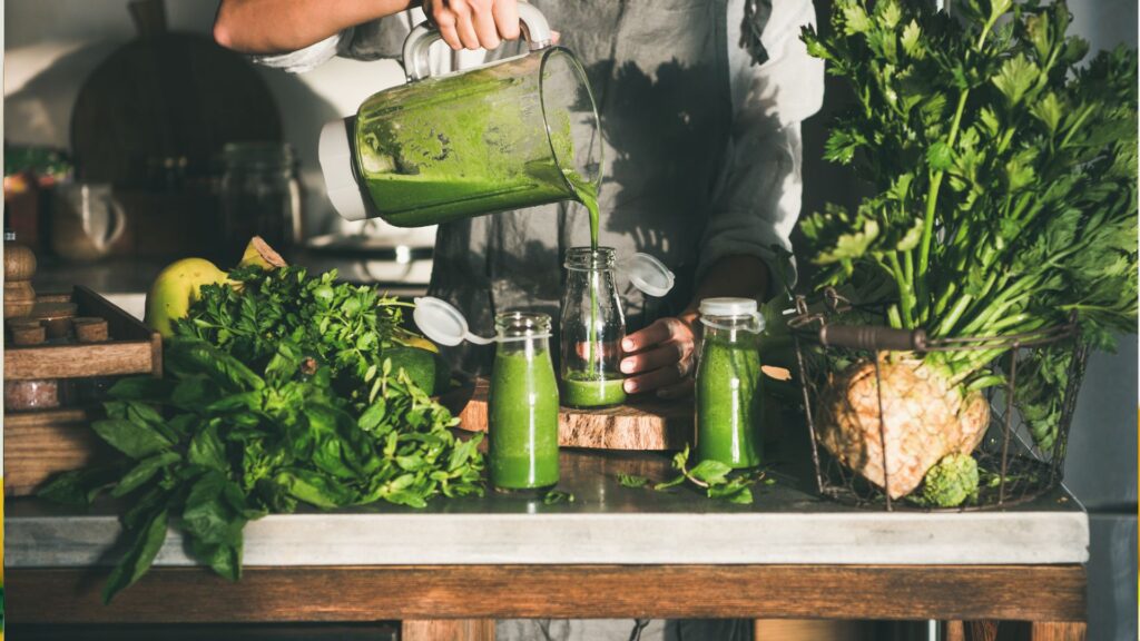 Woman pouring green smoothie from blender to bottle