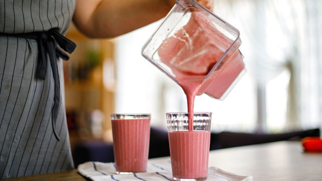 Young woman pouring Strawberry milkshake from blender